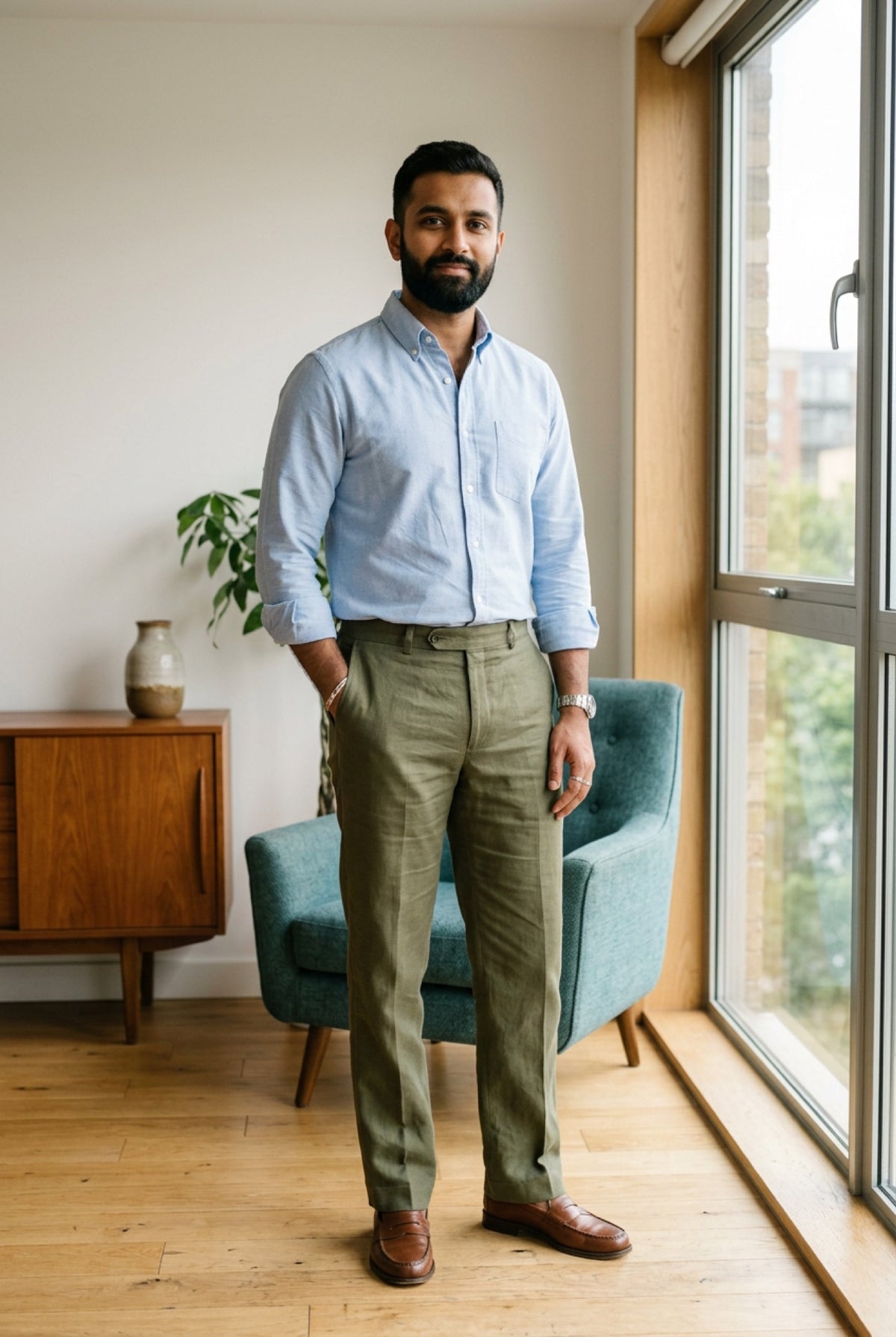 Man in a light blue shirt and olive cotton-linen trousers standing by an office window